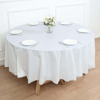 Round table set with a white tablecloth, plates, and a flower vase.