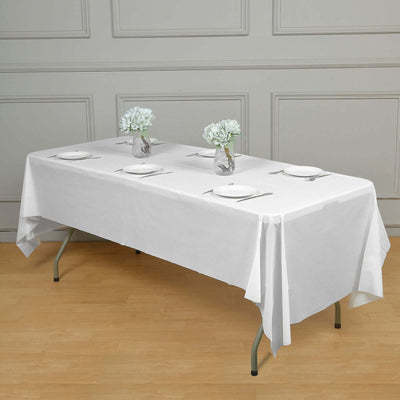 White tablecloth set on a dining table with flowers and plates arranged for a meal.
