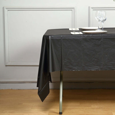 Black tablecloth draped over a table with plates and glasses setting.