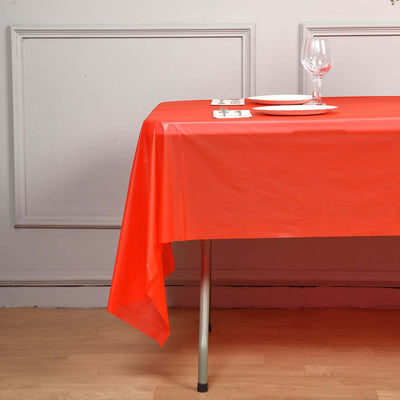 Red tablecloth draped on a table set with plates and a wine glass.