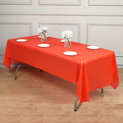 Red tablecloth draped over a table set with plates and vases of flowers.