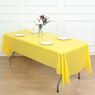 Yellow tablecloth on a dining table set with plates and glasses.