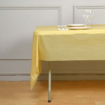 Yellow tablecloth draped over a table with plates and glasses set for dining.