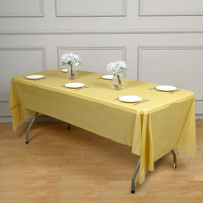Yellow tablecloth on a dining table set with plates and flower vases.