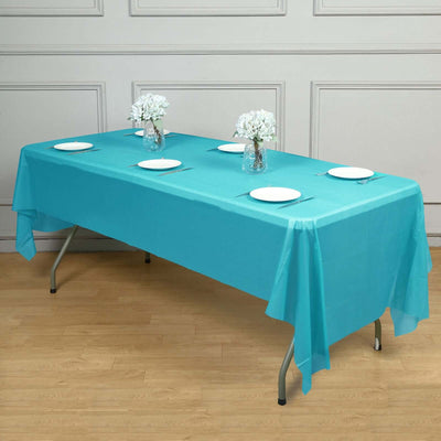 Turquoise tablecloth draped over a table with white plates and vases of flowers.