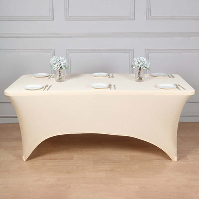 Beige fitted table cover with plates and floral arrangements on a wooden floor.