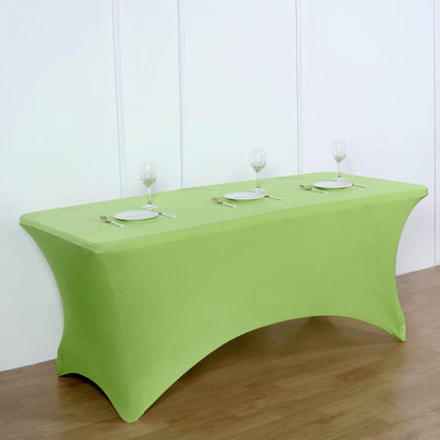 Green tablecloth draped over a rectangular table set for dining with plates and glasses.