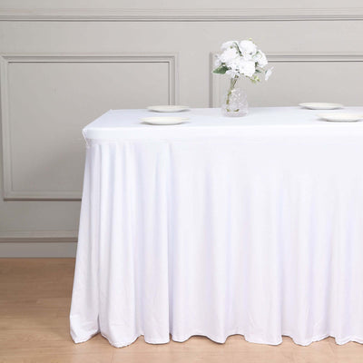 White tablecloth draped over a table with plates and a flower vase.
