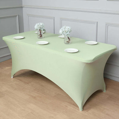 Green fitted table cover with plates and vases on a wooden floor.