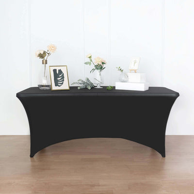 Black fitted table cover on a wooden floor with decorative items on the table.