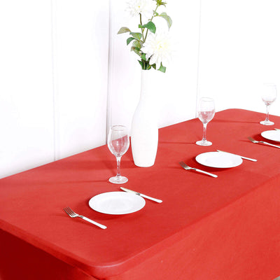 Red tablecloth set with white plates and glassware, featuring a floral centerpiece.
