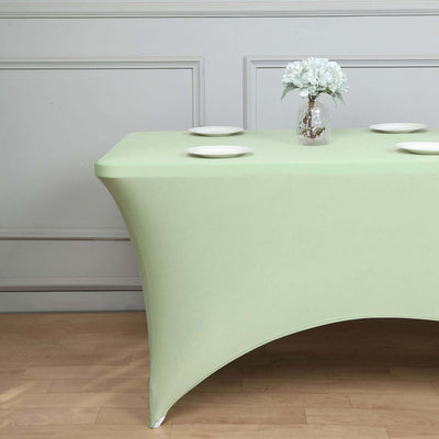 Green fitted table cover with plates and flower vase on a wooden surface.