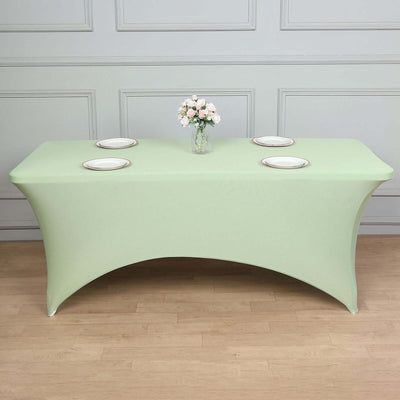 Green fitted table cover with plates and a flower vase on a light wooden surface.