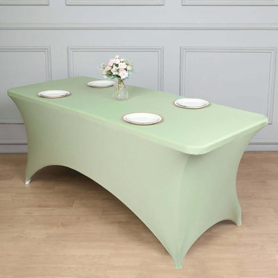 Green fitted table cover with plates and a vase of flowers arranged on a wooden floor.