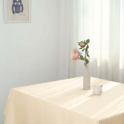 Table setup with a vase of flowers and a cup on a light-colored tablecloth.