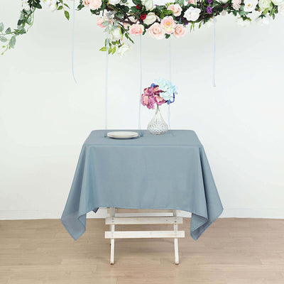 Gray tablecloth draped over a wooden table with flowers and a plate on top.
