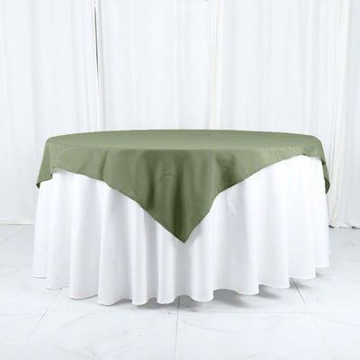 Green tablecloth draped over a round white table in a studio setting.