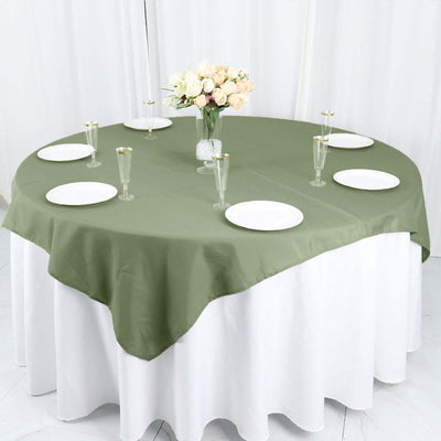 Round olive green tablecloth draped over a circular table with plates and glasses.