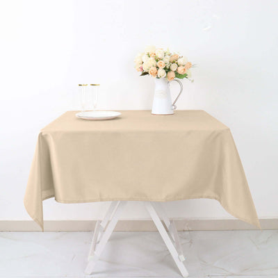 Beige tablecloth draped over a table with flowers and dinnerware.