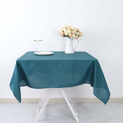 Teal tablecloth on a table with flowers and glasses in a bright setting.