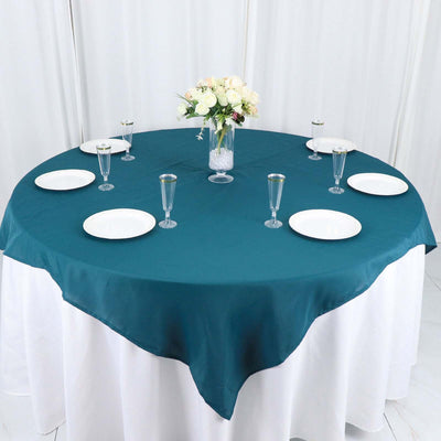 Round teal tablecloth set for dining with white plates and a floral centerpiece.