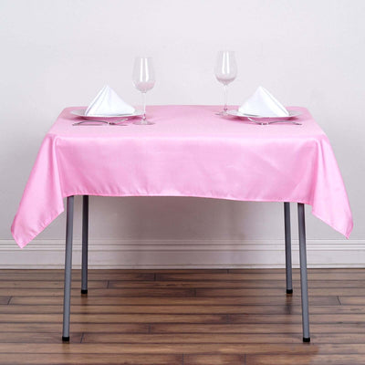 Pink satin tablecloth draped over a table set with glasses and napkins.