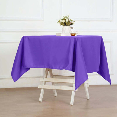 Purple tablecloth draped over a white folding table with a flower vase and tea cup.