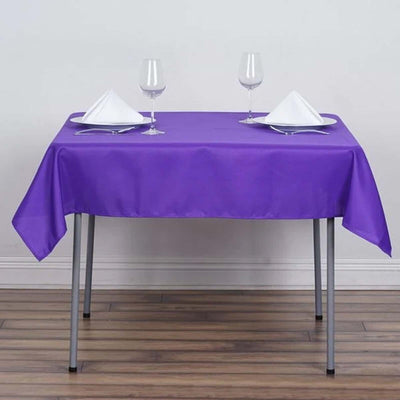 Purple tablecloth set with plates and glasses on a dining table.