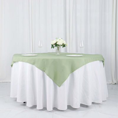 Green tablecloth draped over a round table set for two with a floral centerpiece.