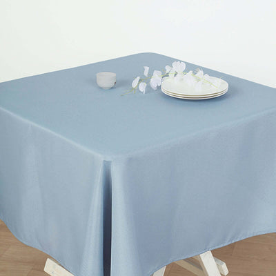 Blue tablecloth on a wooden table with plates and flowers.