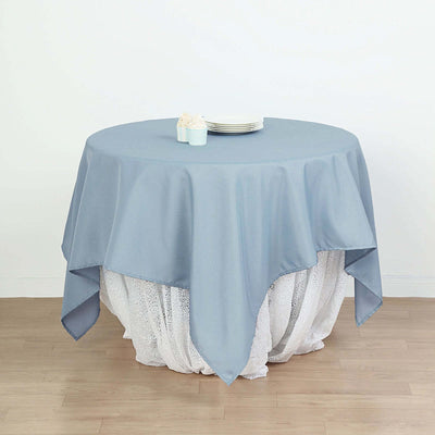 Round blue tablecloth draped over a white table with plates on top.
