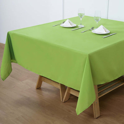 Green tablecloth on a wooden table set with glassware and cutlery.