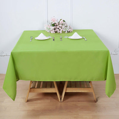 Green tablecloth on a wooden table set for dining with utensils and decor.