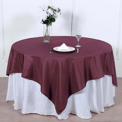 Round burgundy tablecloth draped over a white table with floral centerpiece.