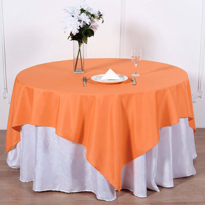 Orange tablecloth draped over a round table with floral centerpiece and glassware.