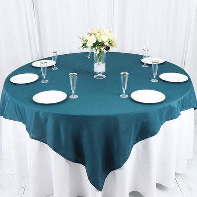 Teal tablecloth on a round table set with plates and glasses, adorned with a flower vase.