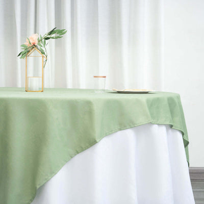 Green tablecloth draped over a white table with a glass and decorative vase.