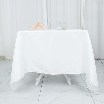 White round table with a tablecloth, glassware, and decorative items.