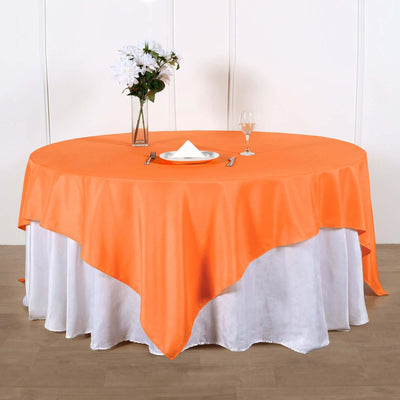 Round orange tablecloth on a dining table set with a plate and glass.