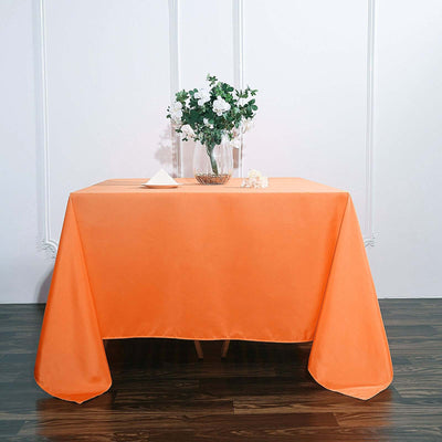 Orange tablecloth draped over a table with a flower vase centerpiece.