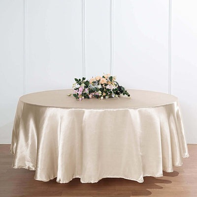 Round satin tablecloth in champagne color with floral arrangement on top.