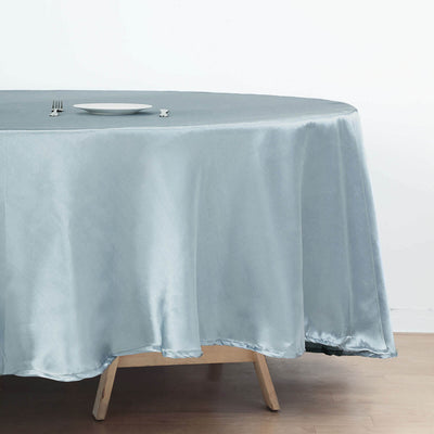 Round light blue tablecloth draped over a wooden table with a plate on top.