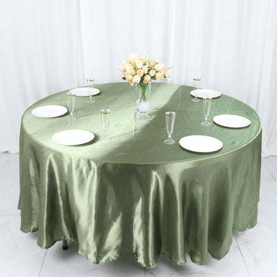 Round green tablecloth set for dining with plates and glasses, adorned with a flower vase.