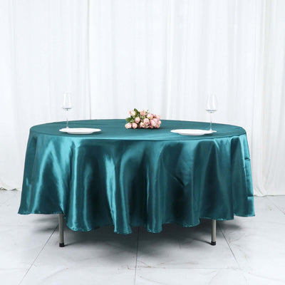Teal satin tablecloth with plates and wine glasses, styled with a floral centerpiece.