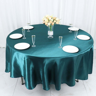 Elegant round table set with teal satin tablecloth and decorative vase of flowers.