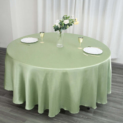 Round green tablecloth on a dining table set with plates and glasses.