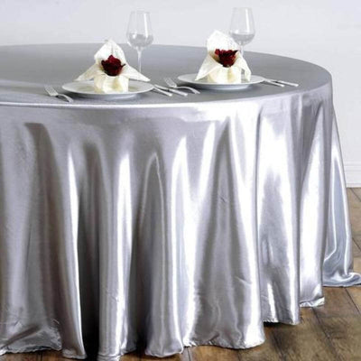 Silver satin tablecloth draped elegantly on a round table with decorative napkins.