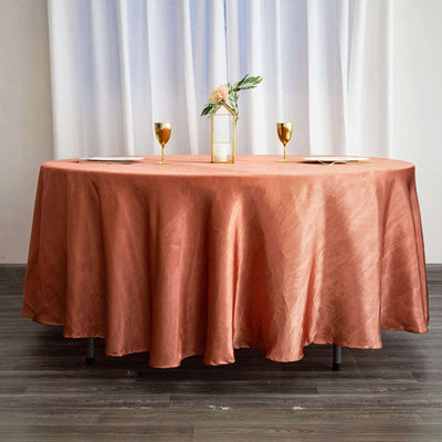 Round coral tablecloth draped over a table with golden glasses and a floral centerpiece.