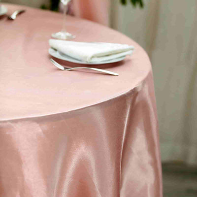 Pink satin tablecloth draped over a round table with silverware and napkin.