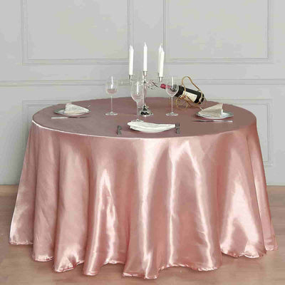 Elegant round table with a satin pink tablecloth, candles, and glassware.